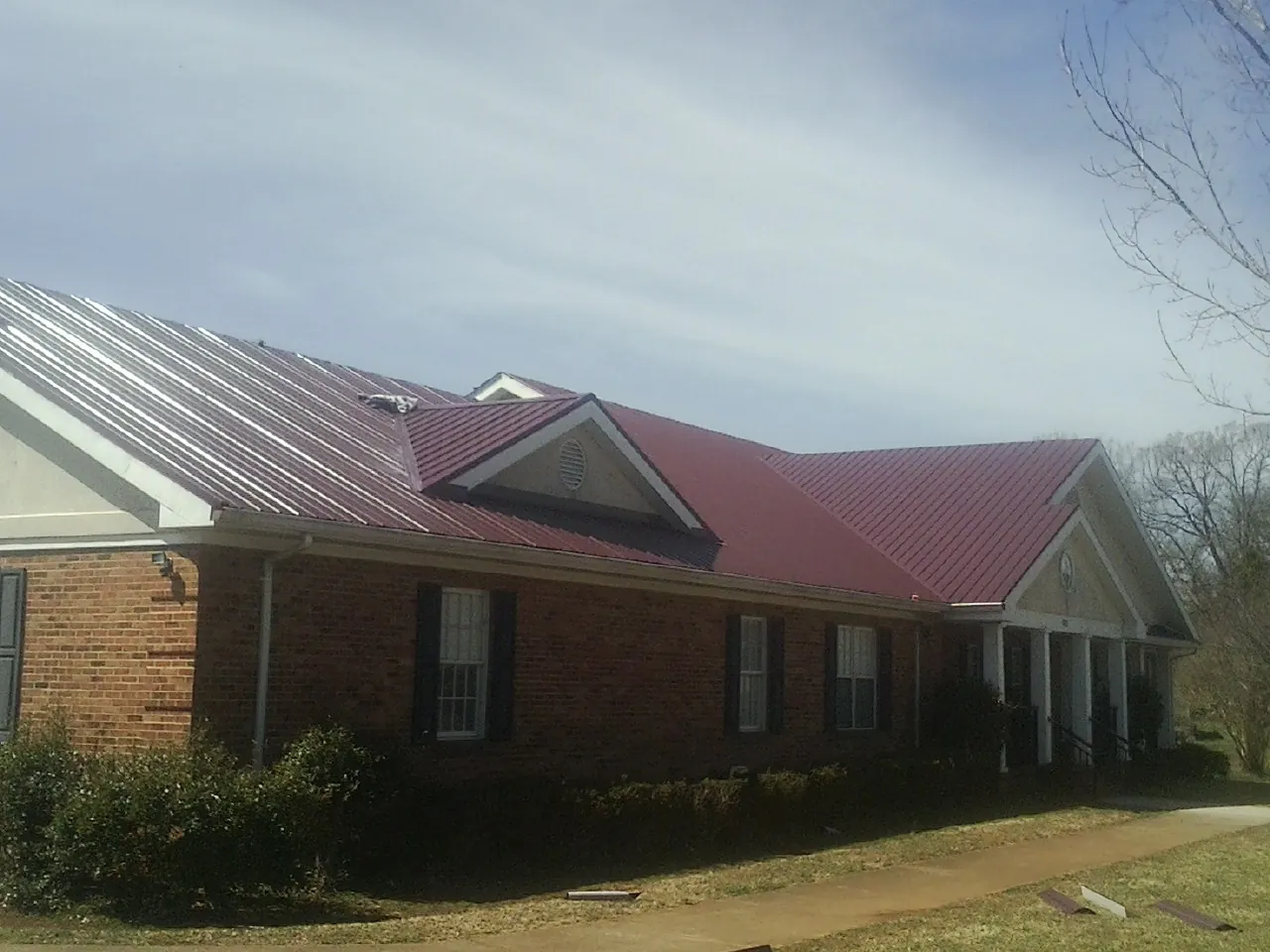 Red metal roof with gabled entries on a long brick building, from a Hail Damage Roof Repair job in Hazleton