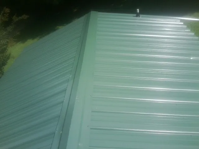 New green metal panels meeting at the ridge of a roof — Flat Roof Repair work by our crew in Hazleton