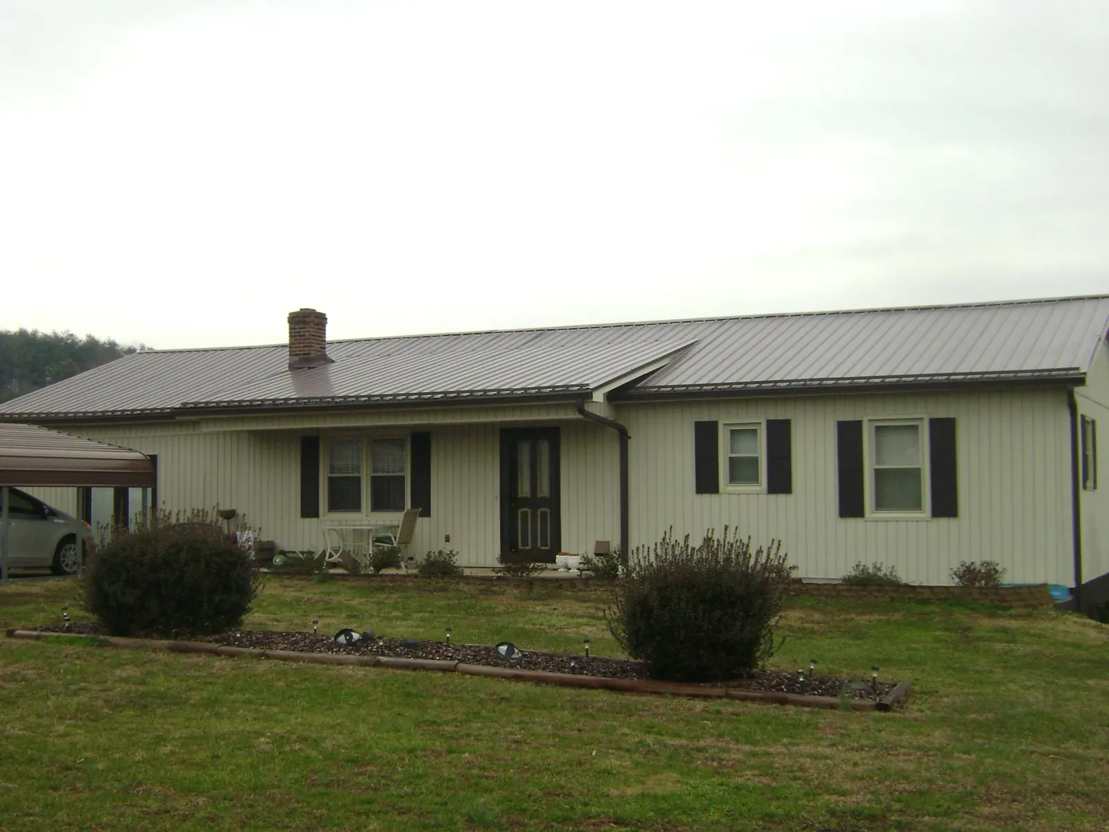 Brown metal roof on a cream sided ranch home with a brick chimney in Hazleton